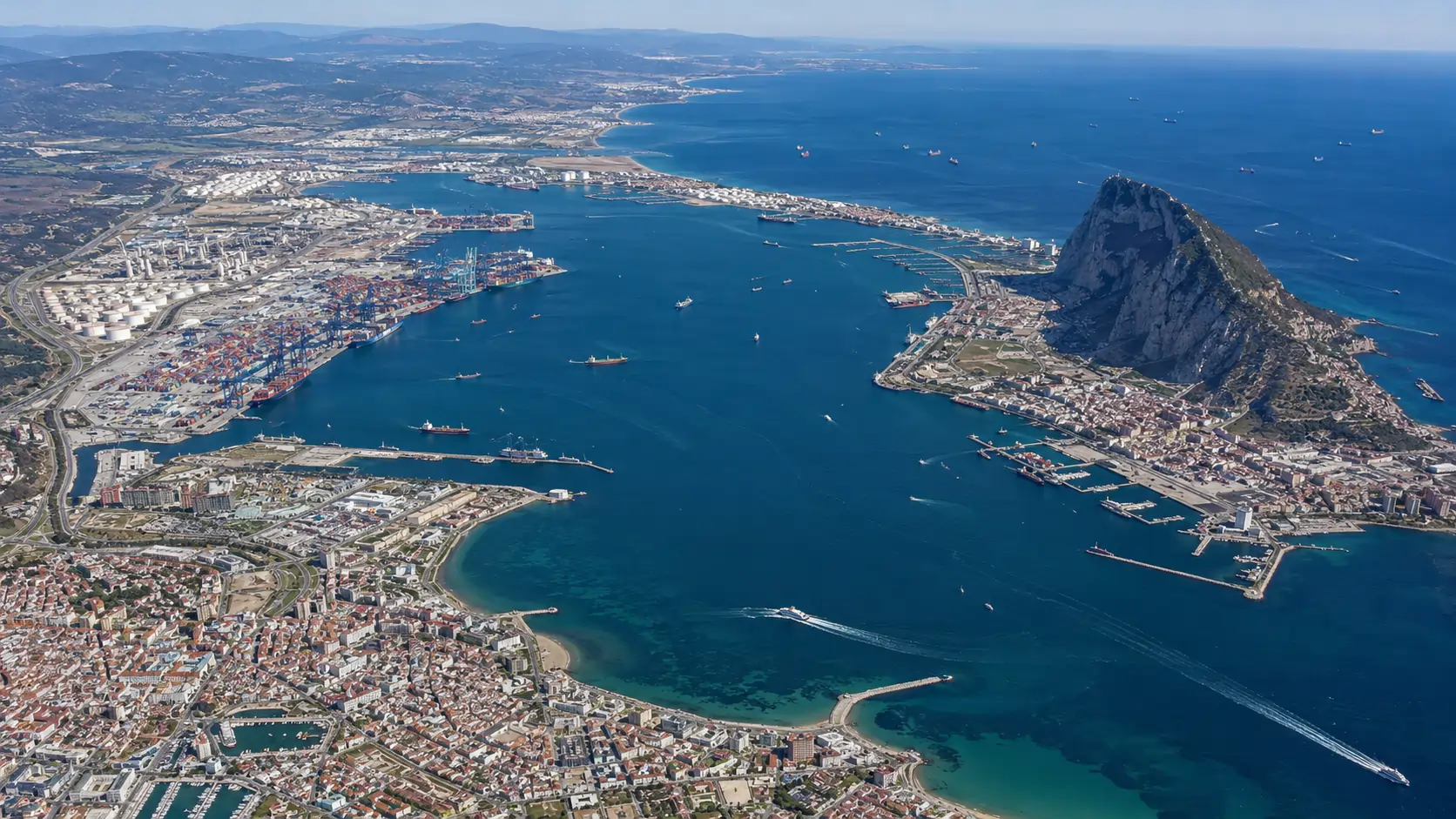 Aerial overview of the Bay of Algeciras port complex showing distributed terminal facilities across the western shore with the Rock of Gibraltar on the east