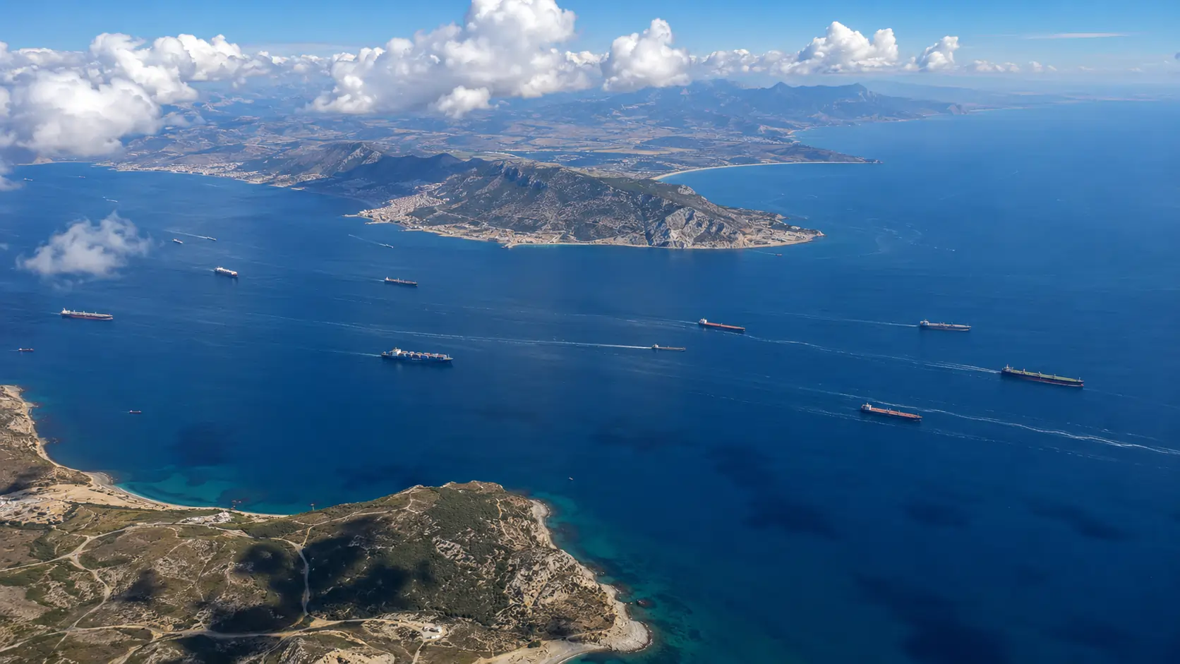 Aerial view of the Strait of Gibraltar showing container vessels and tankers transiting the east-west traffic separation lanes between Spain and Morocco